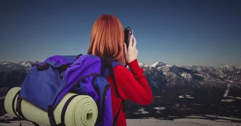 Back of millennial backpacker with camera against snowy mountain range Stock Photos