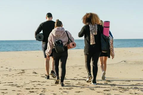 Back of a multicultural group walking on the beach with yoga mats and bags Stock Photos