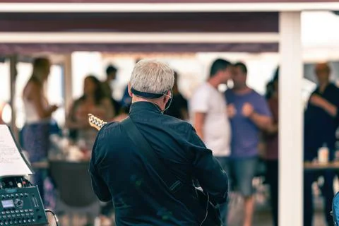 Back of an old man playing the electric guitar on a terrace with public Stock Photos