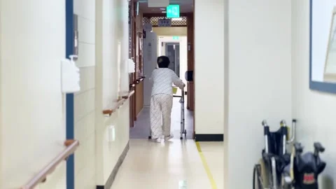 The back of an old man who uses a walking aid to walk through a hospital hallway Stock-Footage 306855379