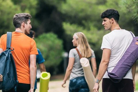 Back of people chatting while holding yoga mats strolling in the forest Stock Photos