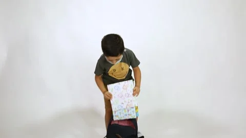 Back to school after Corona - 5 years old boy wearing face mask put colored book Stock Footage 132608543