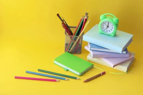 Back to school, alarm clock, stack of books and pencils on bright background Stock Photos