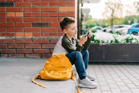 Back to school. Cute child with backpack, holding mobile phone, playing with Stock Photos