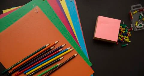 Back to school. Pencils, multi-colored paper and paper clips on a black backg Stock Photos