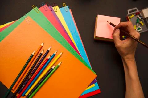 Back to school. Pencils, multi-colored paper and paper clips on a black backg Stock Photos
