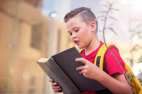 Back to school. Pupil boy with backback reading book outdoor Foto stock