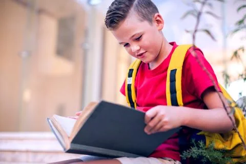 Back to school. Pupil boy with backback reading book outdoor Stock Photos