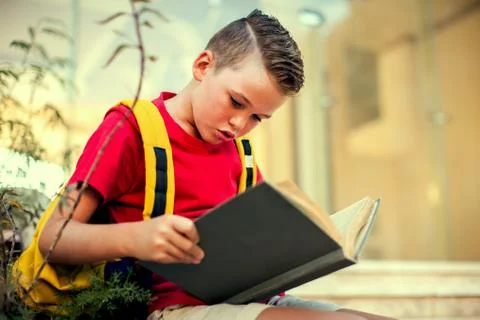 Back to school. Pupil boy with backback reading book outdoor Stock Photos