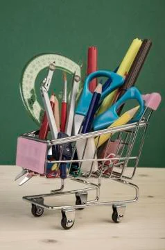 Back to school template with multiple stationery in shopping trolley over gre Stock Photos
