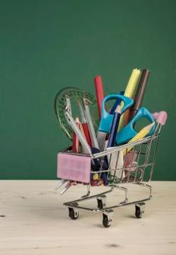 Back to school template with multiple stationery in shopping trolley over gre Stock Photos
