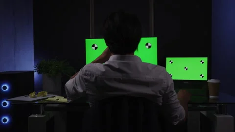 Back shot of an Asian man using a laptop and a monitor with green screens Stock Footage 264223492