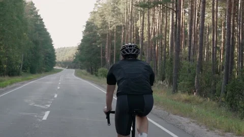 Back shot of man riding a road bike in a forest at the sunset, wearing helmet Stock-Footage 166173962