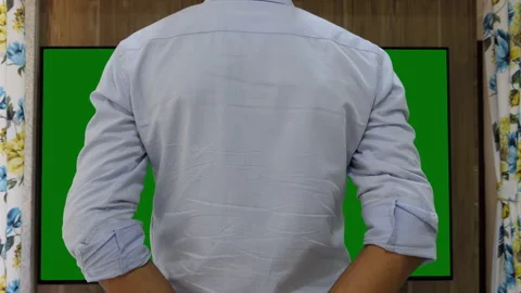 Back shot of a man watching a large green chroma television Stock Footage 147646942