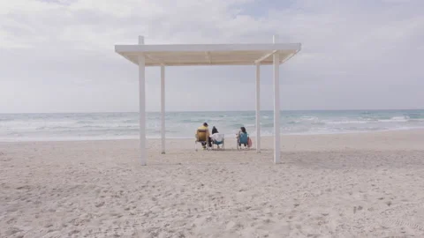 Back shot of persons having rest on the beach, enjoying ocean breeze Stock Footage 229696427