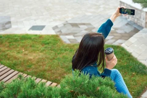 Back shot of an unknown long-haired woman taking picture of herself in park Stock Photos