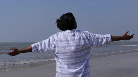 Back shot of a young black man spreading hands at the beach, looking at the sea Stock Footage 147065703