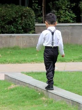Back side of a boy walking in a park. He is wearing formal outfit with suspender Stock Photos