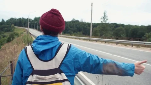 Back side of hiker walking through countryside road hitchhiking cars Stock Footage 80054678