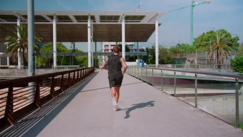 Back side shoot of strong man in black sportswear running at sunny morning urban Video stock 116741133