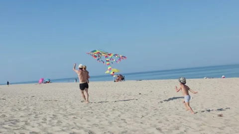 Back side view father and kids flying colorful kite in sky on sunny sandy beach Stock Footage 231300223
