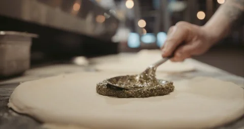 Back of spoon spreading out fresh oil and basil on pizza dough Stock Footage 105299132