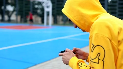 Back of stylish man using smart phone for gaming online on basketball sport area 스톡 동영상 135679911