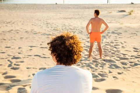 Back turned look away two young men on sandy summer beach. Curly hair man Stock Photos