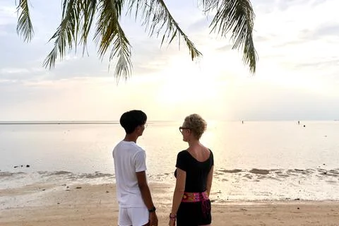 Back of two lovers looking the sunset on the sea from a tropical beach Stock Photos