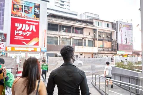 Back of two multiracial friends walking outside a mall with advertising posters Stock Photos