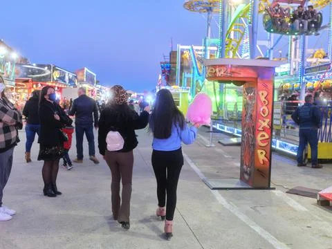 Back of two women strolling while eating a cotton candy at an evening fair Stock Photos