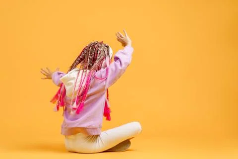 Back view of Adorable child in rounded glasses with pink dreadlocks sitting on Stock Photos