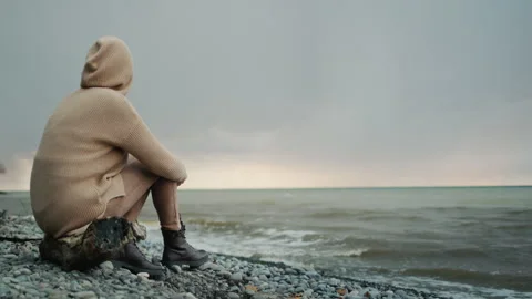 Back view: Alone woman in a warm sweater with a hood on her head sits on the Stock-Footage 246766814