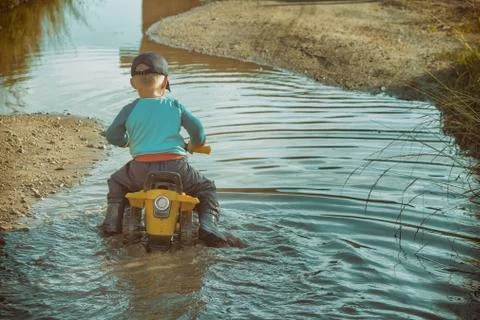 Back view of anonymous boy driving toy transport in dirty brook while playing in Stock Photos