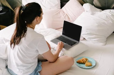 Back view of anonymous woman using laptop on bed Stock Photos