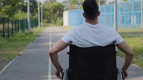 Back view Anonymous Young man rides wheelchair using hands on summer stadium Stock Footage 166339827