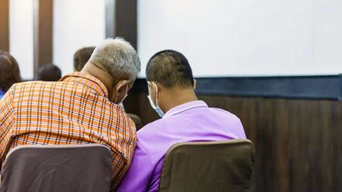 Back view of Asian elderly man in orange shirt wear face mask whisper and t.. Stock Photos