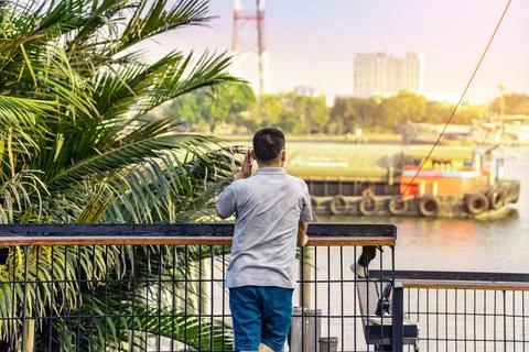 Back view of Asian man using mobile phone to call at riverside. Relax lifesty Stock Photos
