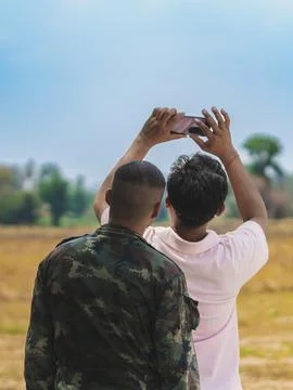 Back view of Asian man using cell phone to take sky photo with army soldier s Stock Photos