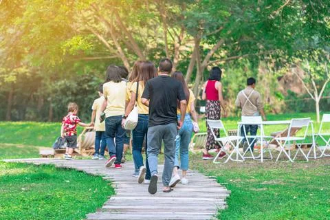 Back view of Asian man walking on pathway through green garden. Group of peop Stock Photos
