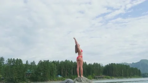 Back view athletic brunette in bikini rising her hands against mountain river. Stockbeeldmateriaal 221766859