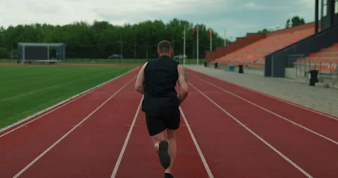 Back view of athletic man sprinting on a red running track at an outdoor stadium Stock Footage 336170618