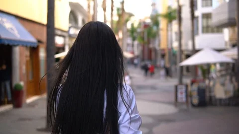 Back view of attractive long-haired curly brunette woman walking down the city Stock Footage 119288400