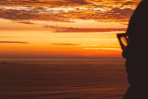 Back view backlight portrait of a single woman watching a sunset on the sea with Stock Photos