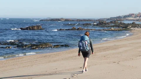 Back view of backpack woman walking alone by sandy wide long beach and enjoying Video stock 323469142