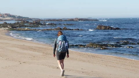 Back view of backpack woman walking alone by sandy wide long beach and enjoying Video stock 335950056