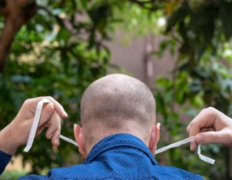 Back view of a bald man putting on a face mask and tying it up behind his hea Stock Photos