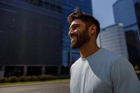 Back view of bearded smiling man in t-shirt standing on skyscrapers background Stock Photos