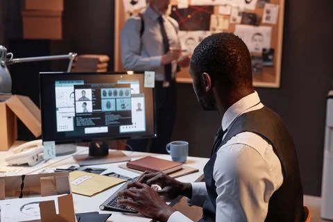 Back view of Black detective using computer at workplace Stock Photos