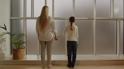 Back view of blond young mom and little daughter looking at panoramic window Stock Footage 243365999